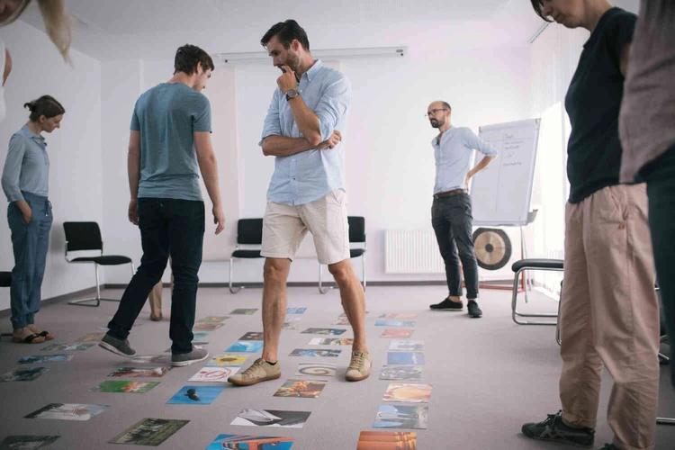 Mann steht in einem raum in mit einer gruppe und schaut auf den boden voller bilder